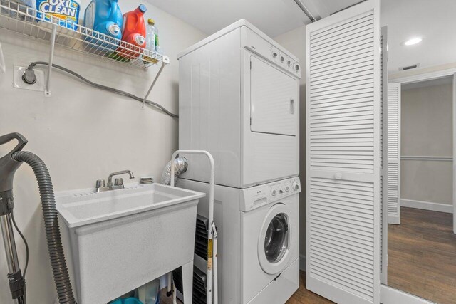 washroom featuring stacked washing maching and dryer, dark hardwood / wood-style flooring, and sink