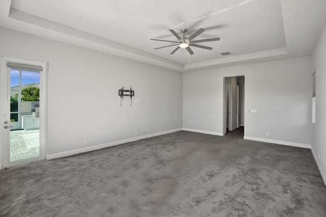 empty room with a tray ceiling, dark carpet, and ceiling fan