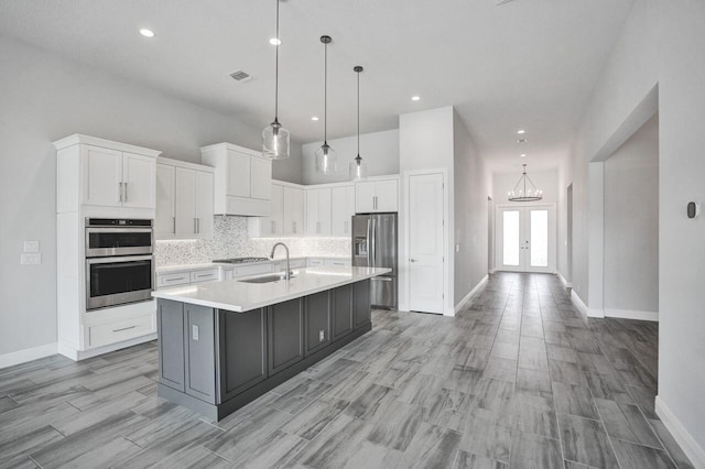 kitchen with white cabinetry, sink, stainless steel appliances, decorative light fixtures, and a kitchen island with sink