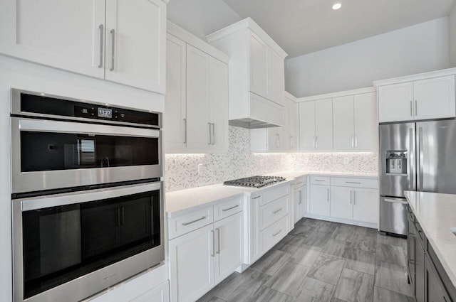 kitchen featuring tasteful backsplash, white cabinetry, stainless steel appliances, and light stone counters