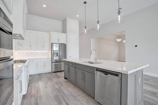 kitchen featuring sink, stainless steel appliances, pendant lighting, a center island with sink, and white cabinets