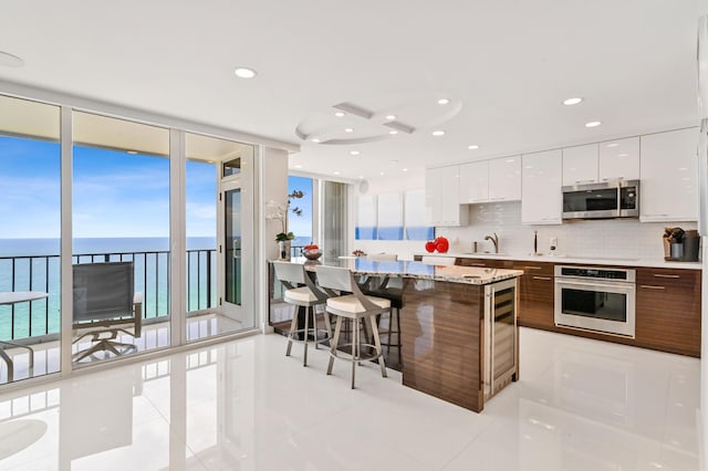 kitchen with appliances with stainless steel finishes, a kitchen bar, a water view, a center island, and white cabinets