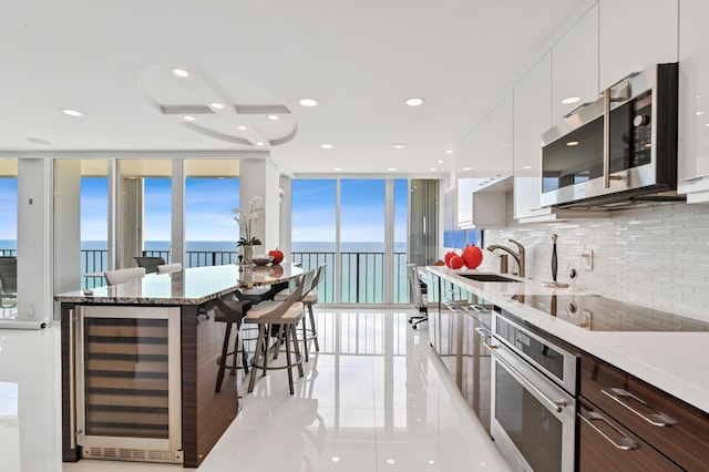 kitchen with a water view, sink, appliances with stainless steel finishes, white cabinets, and beverage cooler