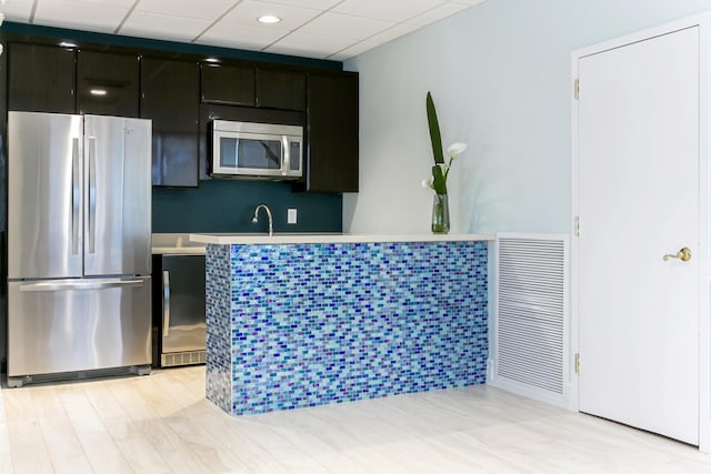 kitchen featuring light hardwood / wood-style floors, appliances with stainless steel finishes, sink, and a drop ceiling