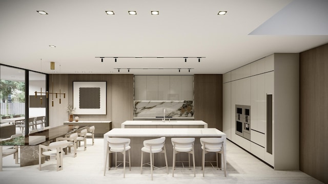 kitchen featuring a kitchen island with sink, a kitchen breakfast bar, rail lighting, expansive windows, and white cabinetry