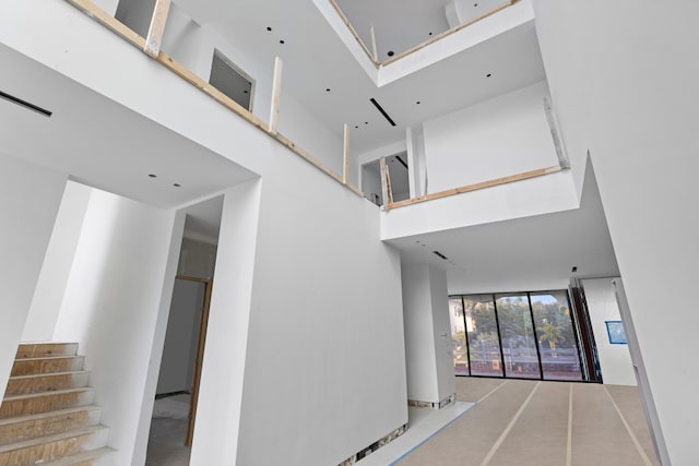 corridor featuring stairway, a high ceiling, and expansive windows