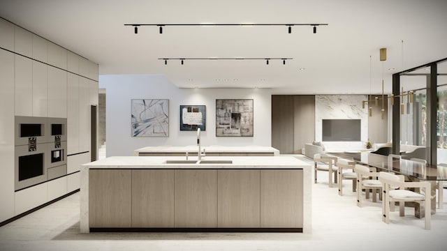 kitchen featuring an island with sink, sink, rail lighting, white cabinets, and decorative light fixtures