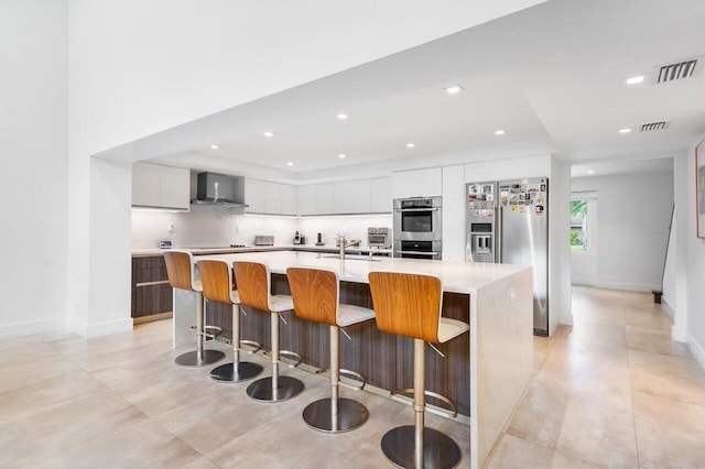 kitchen with a kitchen island with sink, appliances with stainless steel finishes, decorative backsplash, and wall chimney range hood