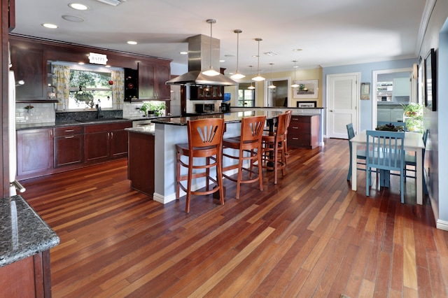 kitchen with tasteful backsplash, dark wood-type flooring, decorative light fixtures, a large island, and island range hood