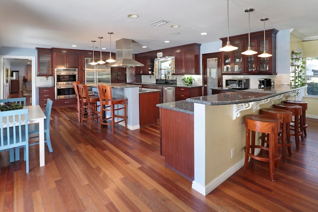 kitchen with hanging light fixtures, a kitchen island, island range hood, appliances with stainless steel finishes, and dark hardwood / wood-style flooring