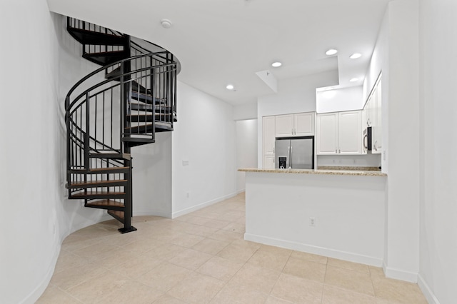 kitchen with white cabinetry, stainless steel appliances, light stone countertops, and kitchen peninsula