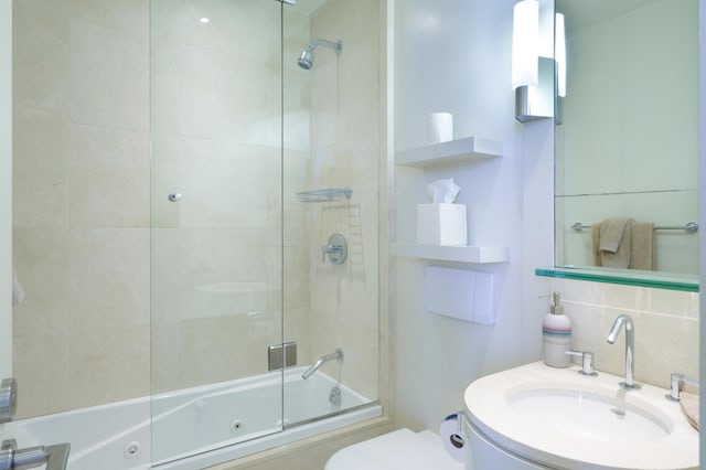 full bathroom featuring bath / shower combo with glass door, vanity, backsplash, and toilet