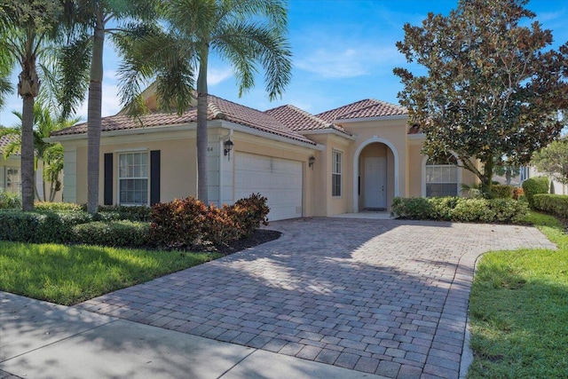 mediterranean / spanish-style house featuring a garage, decorative driveway, a tiled roof, and stucco siding