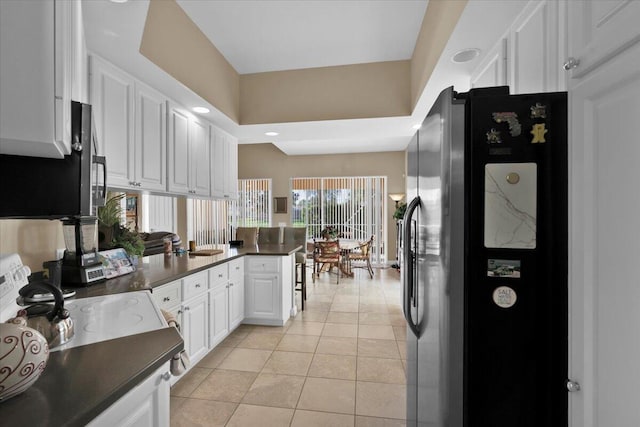 kitchen featuring light tile patterned floors, white cabinets, dark countertops, a peninsula, and fridge with ice dispenser