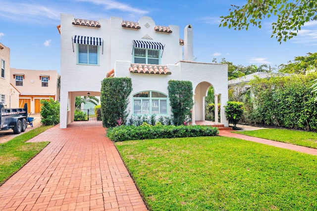 mediterranean / spanish-style house with stucco siding, a tile roof, a front yard, and a gate