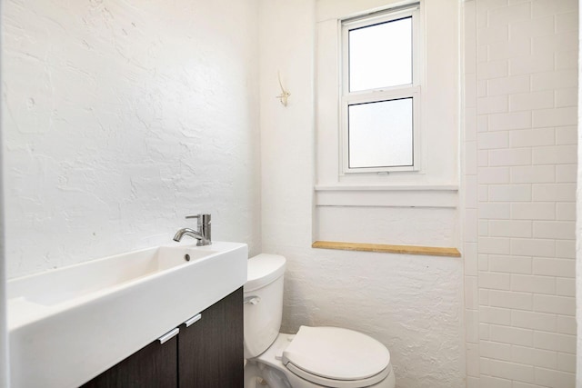 bathroom featuring toilet, vanity, and a textured wall