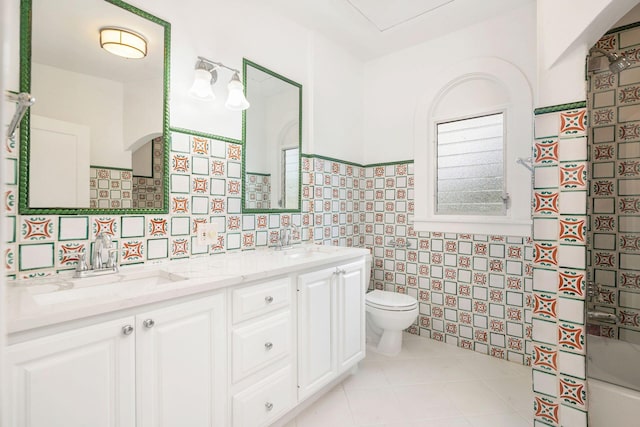 full bath with tile patterned flooring, tile walls, toilet, and a sink