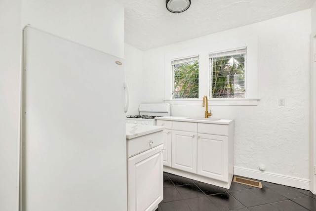 interior space featuring visible vents, a sink, white appliances, white cabinetry, and dark tile patterned flooring