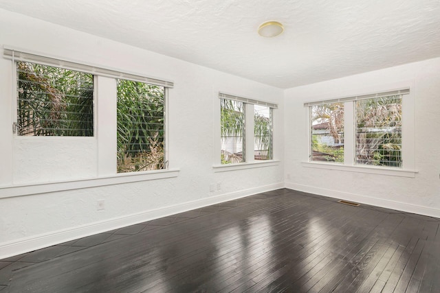 unfurnished room with a textured wall, a textured ceiling, baseboards, and dark wood-style flooring