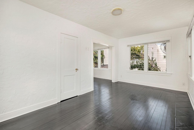 empty room featuring baseboards, a textured ceiling, dark wood-style flooring, and a textured wall