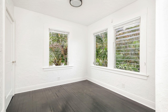 empty room featuring a textured wall, baseboards, and dark wood-style flooring