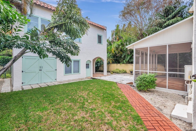 back of house featuring fence, a tiled roof, stucco siding, a yard, and a sunroom