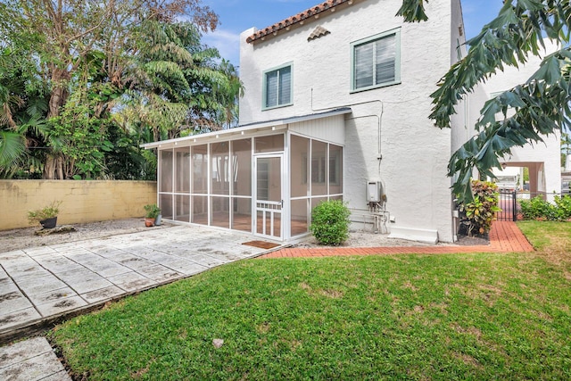 rear view of property with a yard, fence, a sunroom, and stucco siding