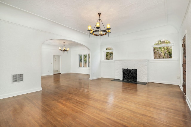 unfurnished living room with a notable chandelier, visible vents, wood finished floors, and a high end fireplace