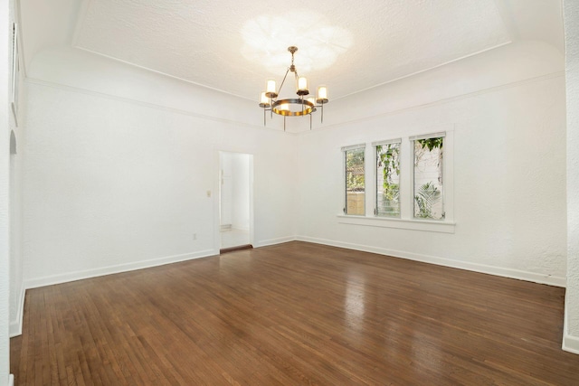 spare room featuring an inviting chandelier, wood finished floors, baseboards, and a textured ceiling