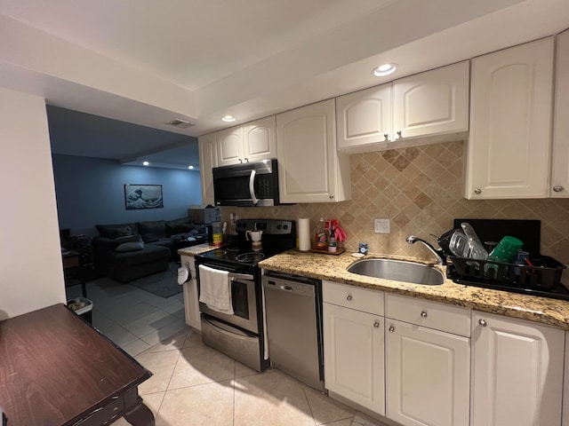 kitchen featuring white cabinets, light tile patterned floors, appliances with stainless steel finishes, light stone counters, and sink