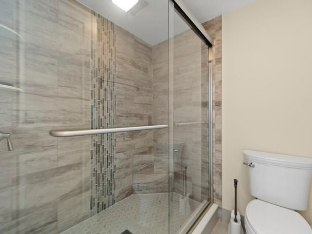 bathroom featuring toilet and a shower with shower door