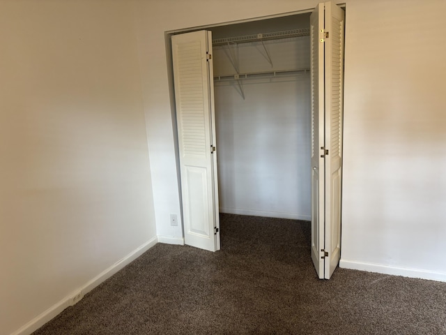 unfurnished bedroom with dark colored carpet and a closet