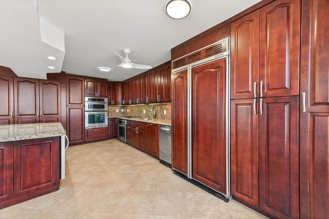 kitchen featuring ceiling fan, stainless steel appliances, a center island, light stone counters, and tasteful backsplash