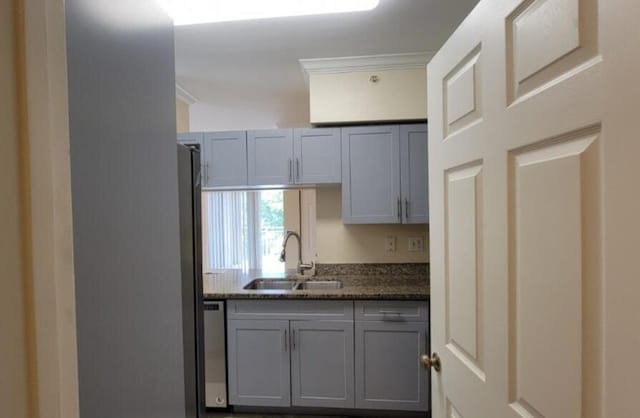 kitchen with gray cabinetry, stainless steel dishwasher, ornamental molding, sink, and dark stone countertops