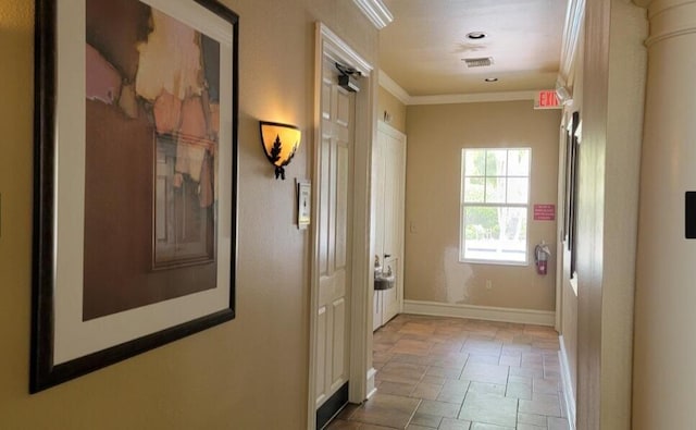 hallway featuring ornamental molding, stone finish floor, visible vents, and baseboards