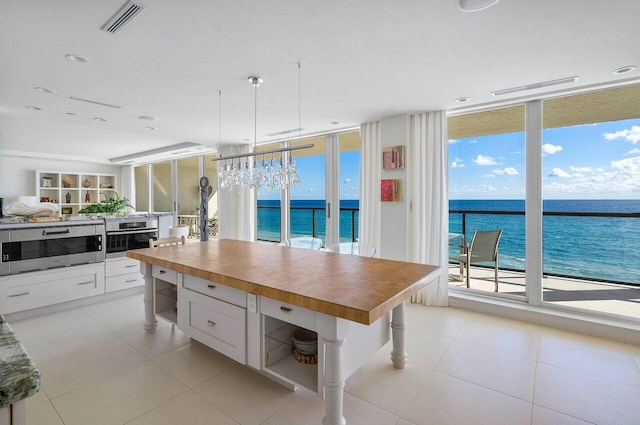 kitchen with floor to ceiling windows, a water view, appliances with stainless steel finishes, pendant lighting, and white cabinets