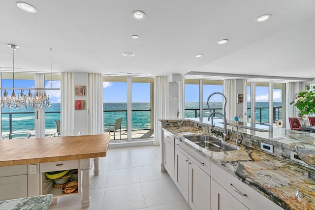 kitchen with sink, a water view, expansive windows, a healthy amount of sunlight, and white cabinets