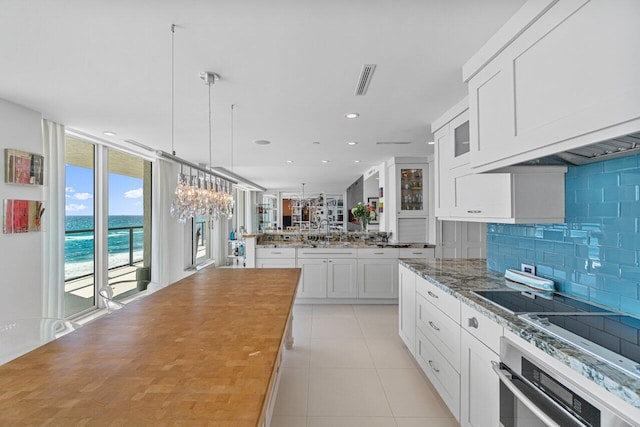 kitchen with a water view, stainless steel oven, white cabinets, pendant lighting, and backsplash