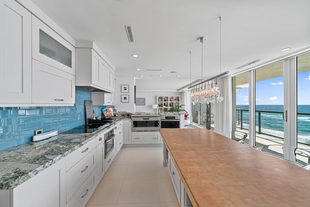 kitchen with pendant lighting, white cabinetry, expansive windows, a water view, and black electric cooktop