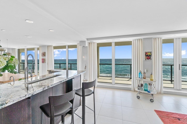 kitchen featuring a breakfast bar, light tile patterned floors, a water view, floor to ceiling windows, and light stone countertops