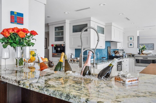 kitchen featuring light stone counters, appliances with stainless steel finishes, custom exhaust hood, and white cabinets