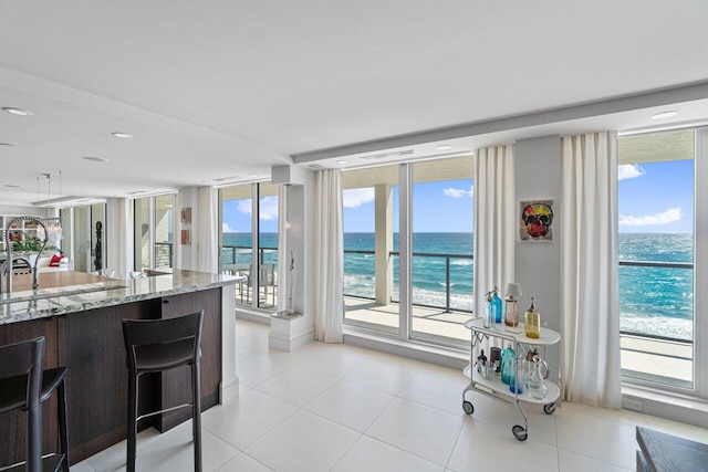 kitchen with light tile patterned flooring, a view of the beach, expansive windows, light stone counters, and a water view