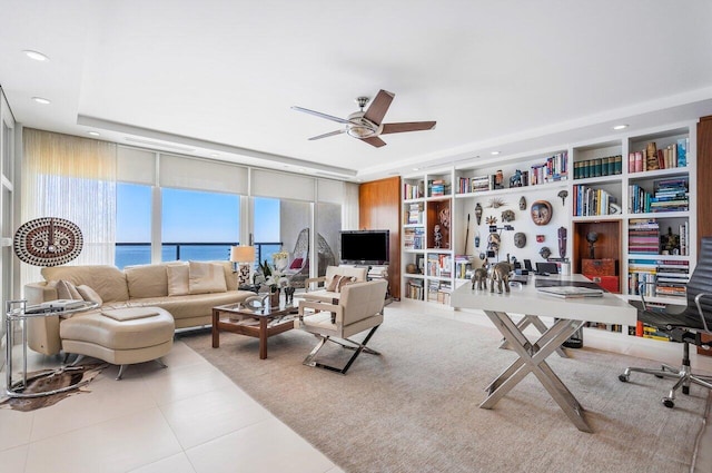 tiled living room with built in shelves, ceiling fan, and a raised ceiling