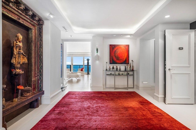 hall with light tile patterned flooring, a water view, and a tray ceiling