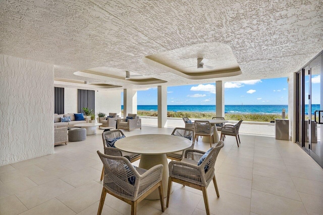 dining room with a water view, a wall of windows, a beach view, and a tray ceiling