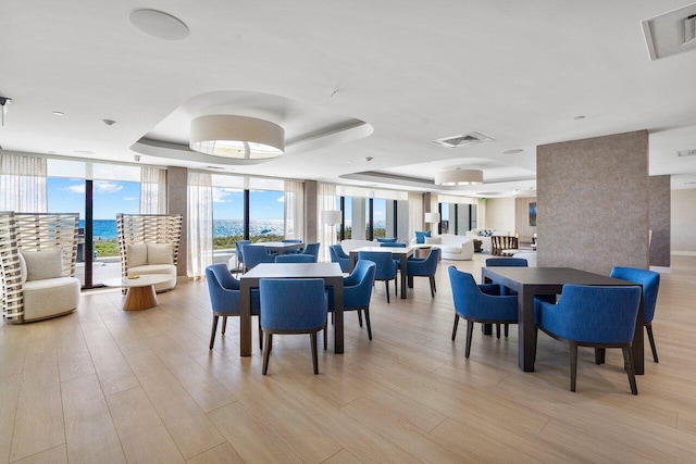 dining space with floor to ceiling windows, a raised ceiling, and light wood-type flooring