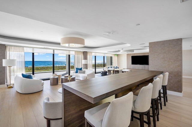 dining room with floor to ceiling windows, a water view, light wood-type flooring, and a tray ceiling