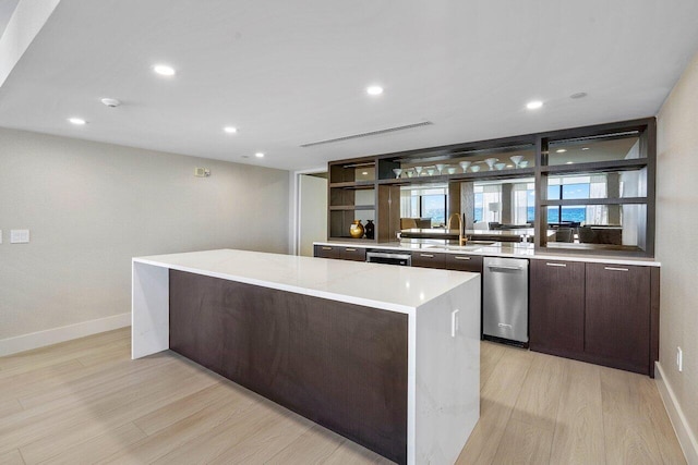 kitchen featuring light stone countertops, a kitchen island, sink, and light wood-type flooring