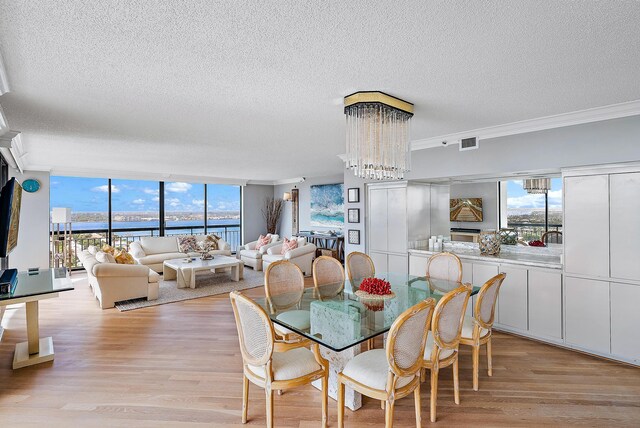 dining room with a water view, light hardwood / wood-style flooring, ornamental molding, a textured ceiling, and a notable chandelier