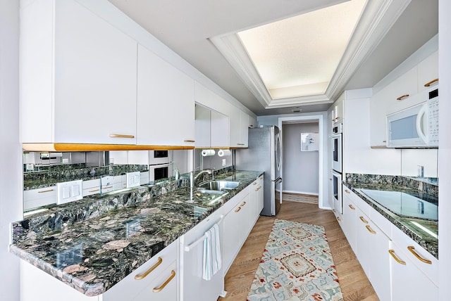 kitchen featuring appliances with stainless steel finishes, white cabinetry, a raised ceiling, and dark stone countertops